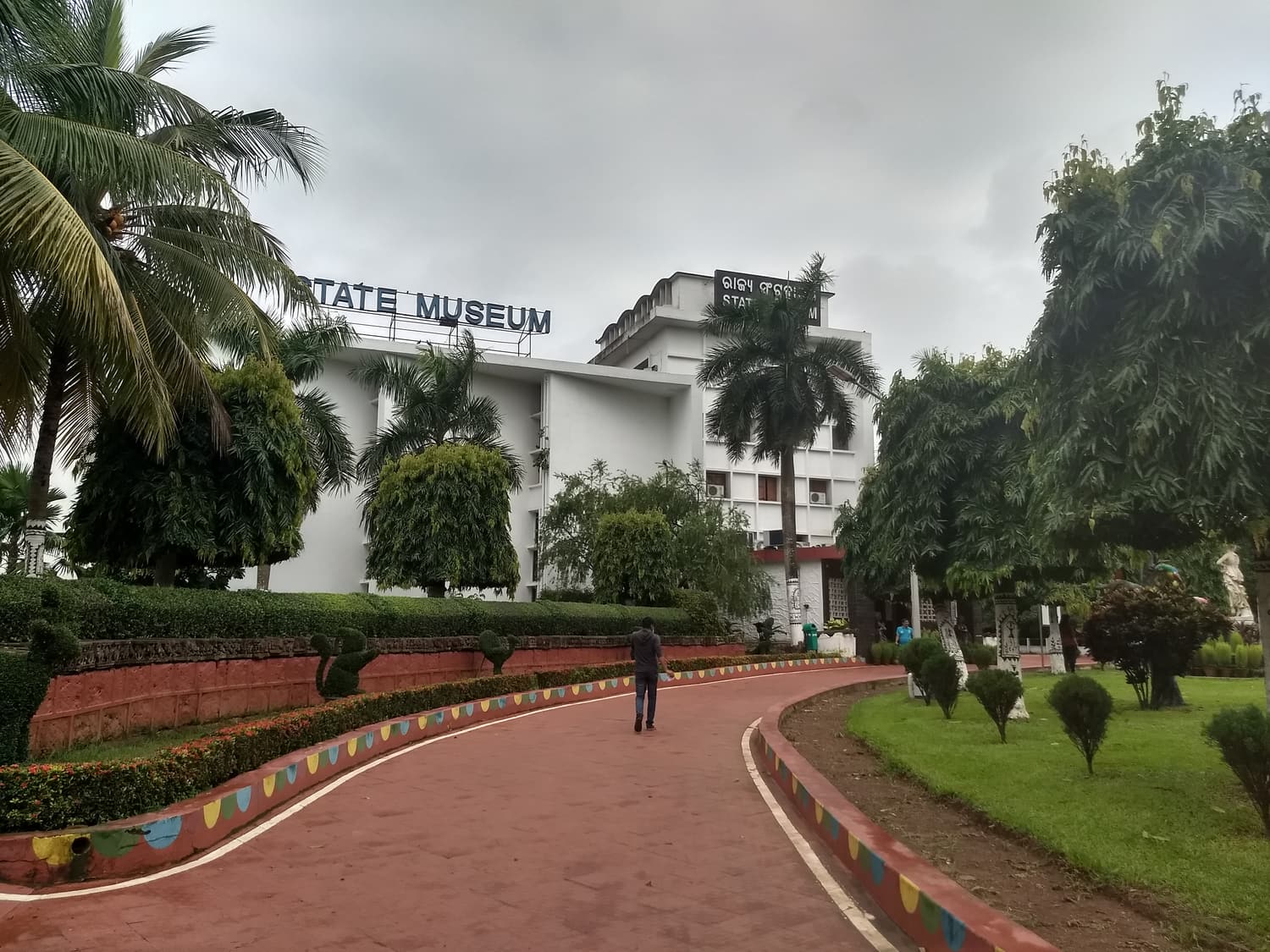 The white Odisha State Museum building behind palm trees and a curving drive